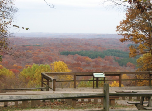 Scenic view of a colorful autumn landscape from a wooden overlook, featuring trees in shades of orange, yellow, and green.