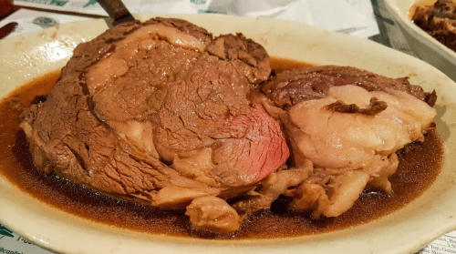 A plate of tender, juicy roast beef in a rich brown gravy, showcasing marbled meat and a side of fat.