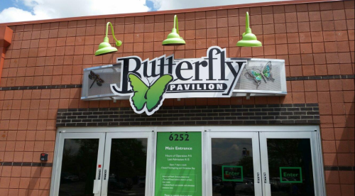 Sign for the Butterfly Pavilion featuring green and black butterflies, with a main entrance below.