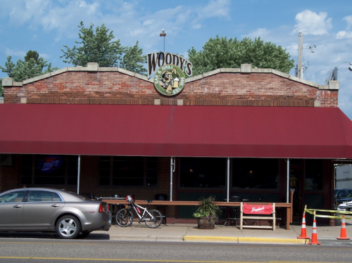 Exterior of Woody's Grill, featuring a red awning, a parked car, a bicycle, and a sign on a brick building.