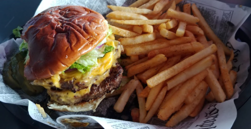 A juicy cheeseburger with lettuce and onions, served with a side of golden French fries on a paper-lined plate.