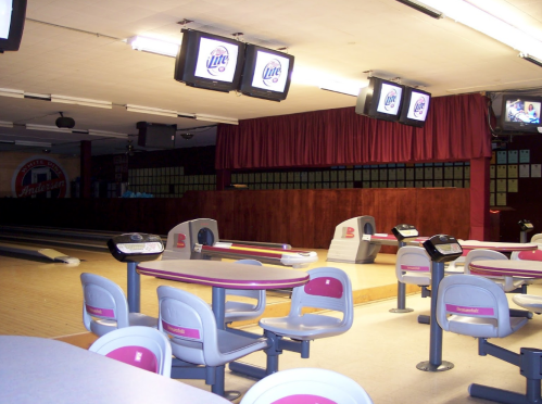 Interior of a bowling alley featuring empty lanes, tables, and screens displaying advertisements.