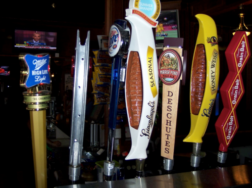 A row of beer taps featuring various brands and styles, with a TV screen in the background.