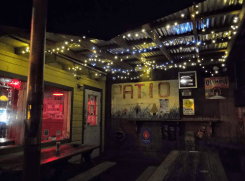 Cozy outdoor patio at night, adorned with string lights and rustic decor, featuring wooden tables and a welcoming atmosphere.
