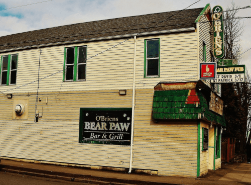Exterior of O'Brien's Bear Paw Bar & Grill, featuring a green shingled roof and a vintage sign.