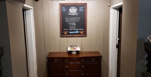 A wooden dresser with a dessert display, flanked by two doorways and a chalkboard sign reading "Bakery This Way."