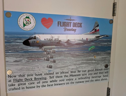Sign promoting Flight Deck Brewing, featuring an aircraft and parachutes, inviting visitors to enjoy local craft beer.