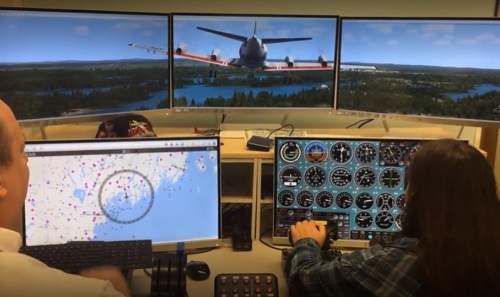 Two people operate a flight simulation setup with multiple screens displaying an aircraft and navigation data.