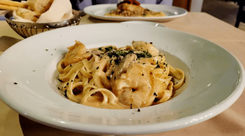 A plate of creamy fettuccine pasta topped with chicken and herbs, served in a white bowl on a table.