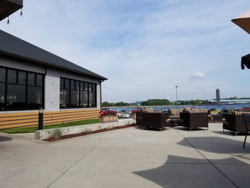 Outdoor seating area with wicker chairs, a view of water, and a modern building under a partly cloudy sky.