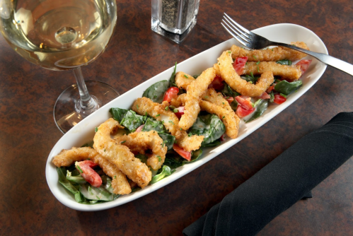 A plate of crispy fried calamari on a bed of salad, accompanied by a glass of white wine.