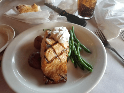 Grilled salmon fillet with a dollop of sauce, served with red potatoes and green beans on a white plate.