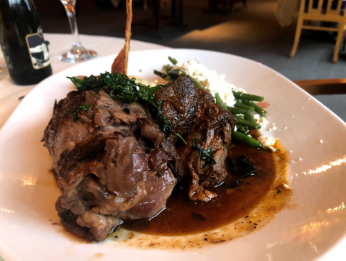 A plated dish featuring tender meat with herbs, served with green beans and a side of creamy white garnish.