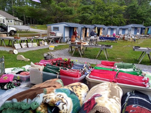A vibrant outdoor market with colorful blankets in the foreground and various stalls in the background.