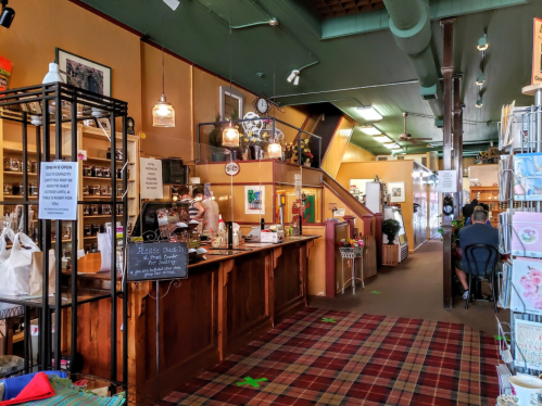 A cozy shop interior with wooden counters, decorative items, and a checkered rug, featuring customers and staff.