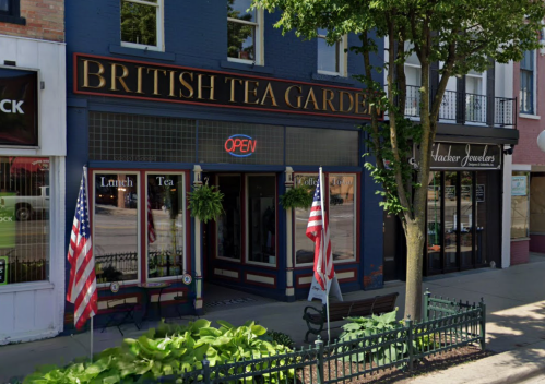 Exterior of British Tea Garden with "OPEN" sign, flags, and greenery outside. Nearby jewelry store visible.
