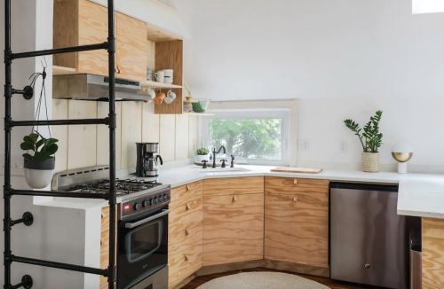 Modern kitchen with wooden cabinetry, a gas stove, and a window, featuring plants and minimalist decor.