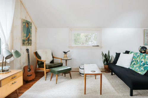 Cozy living space with a green chair, black sofa, wooden table, plants, and artwork on the walls. Bright and inviting atmosphere.