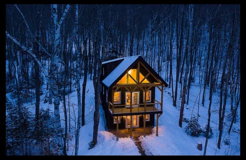 A cozy cabin with warm lights, surrounded by snow-covered trees in a serene winter landscape.