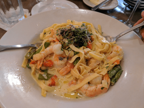 A plate of fettuccine pasta with shrimp, asparagus, and a creamy sauce, garnished with microgreens.
