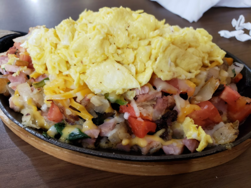 A sizzling skillet filled with diced ham, vegetables, cheese, and topped with fluffy scrambled eggs.