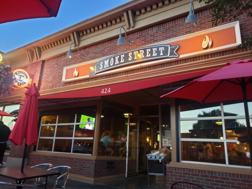 Exterior of Smoke Street restaurant with a red awning, outdoor seating, and a brick facade, under a clear blue sky.