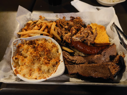 A platter of barbecue featuring pulled pork, brisket, sausage, fries, cornbread, and mac and cheese.