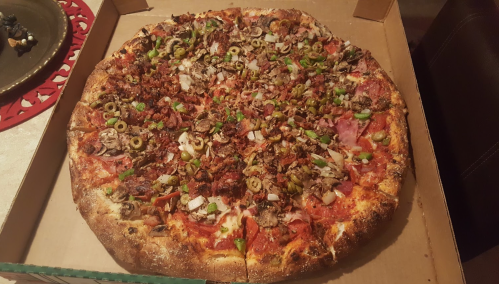 A large pizza topped with various meats, olives, onions, and green peppers in a pizza box.
