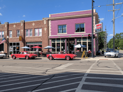 A vibrant purple building with outdoor seating, classic red cars parked nearby, and a clear blue sky above.