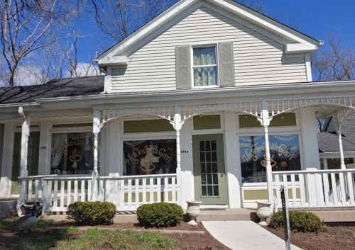 A charming white house with green shutters, featuring a porch and large windows displaying "The Plan with Geri."