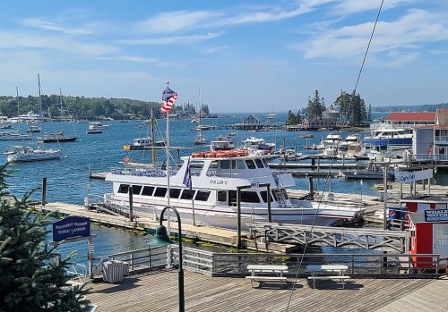 A scenic harbor with boats docked, featuring a large white vessel and an American flag, under a clear blue sky.