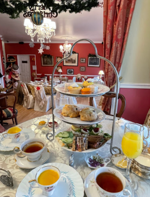 A beautifully set tea room with a tiered stand of pastries, scones, and tea cups on elegant tables.