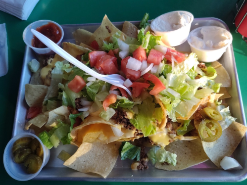 A tray of nachos topped with cheese, lettuce, tomatoes, jalapeños, and served with salsa and sour cream on the side.