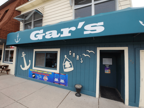 A storefront with a blue awning reading "Gar's," featuring nautical decorations and a sign for games and drinks.