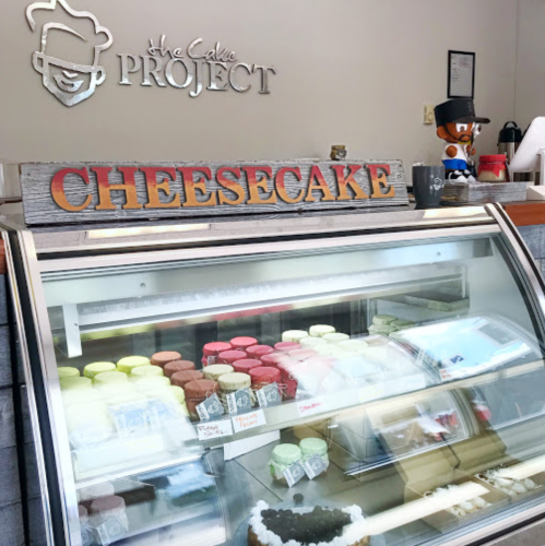 Display case at a dessert shop featuring various cheesecakes and colorful treats, with a sign reading "Cheesecake."