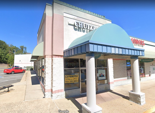 Exterior view of a restaurant with a blue awning, large windows, and a sign for catering services. Parking lot visible.