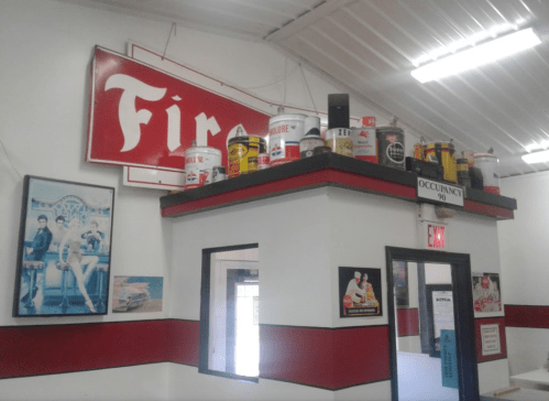 A room with a "Fire" sign, vintage posters, and various colorful paint cans displayed on top of a partition.
