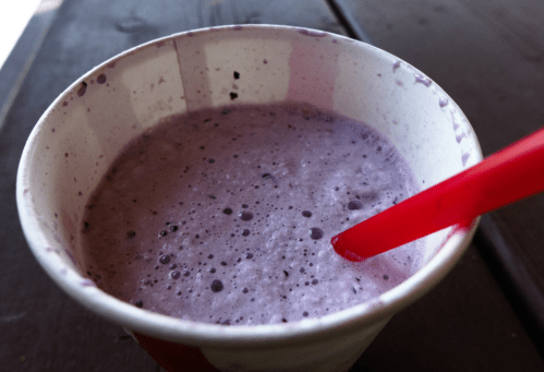 A cup of purple smoothie with a red straw, resting on a wooden table.