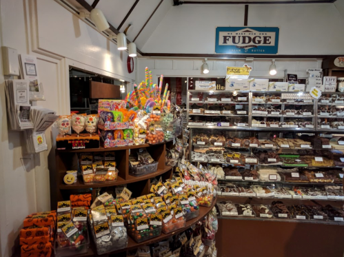 A cozy candy shop filled with colorful sweets, fudge, and various confections displayed on shelves and counters.