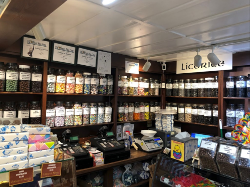 A colorful candy shop interior with jars of sweets on shelves, cash registers, and various candy displays.