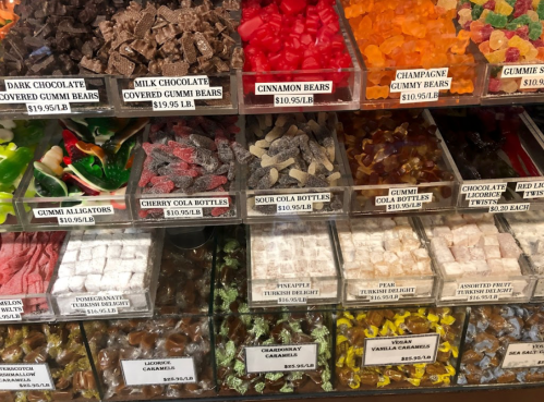 A colorful display of various candies in clear containers, including gummies, chocolate, and sour treats.