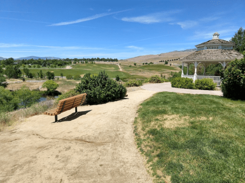 A scenic park view featuring a bench, gazebo, and rolling hills under a clear blue sky.