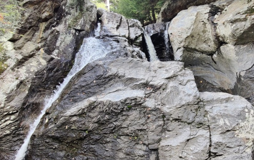 A rocky waterfall cascading down a steep cliff surrounded by trees.