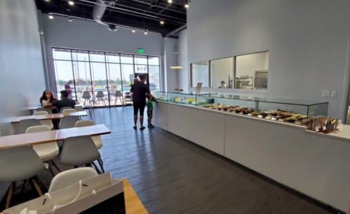 A modern dessert shop interior with a display case, tables, and large windows letting in natural light.