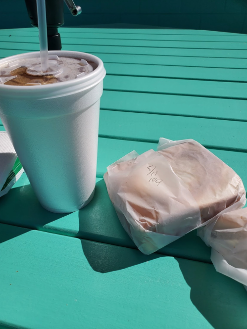 A white cup with a straw next to two wrapped sandwiches on a turquoise table.