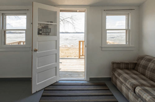 A cozy room with a door open to a view of a lake, featuring a couch and a striped rug.