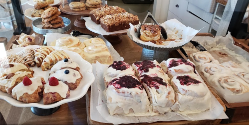 A variety of baked goods displayed on tables, including cinnamon rolls, pastries, and cookies.