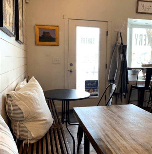 Cozy bakery interior with wooden tables, striped cushions, and a door leading outside.