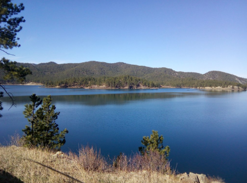 A serene lake surrounded by green hills and trees under a clear blue sky.