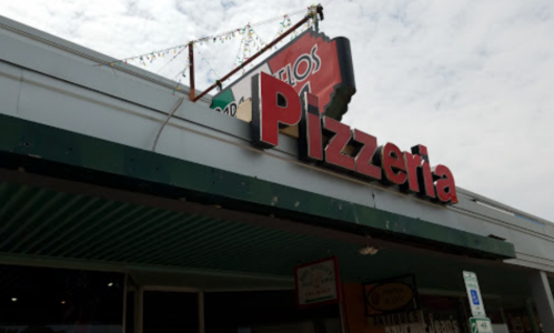 Sign for a pizzeria on a storefront, with decorative lights above and a cloudy sky in the background.